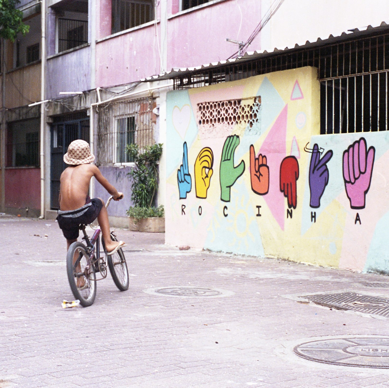 uma criança de bicicleta na frente de um mural onde ROCINHA está escrito em Libras