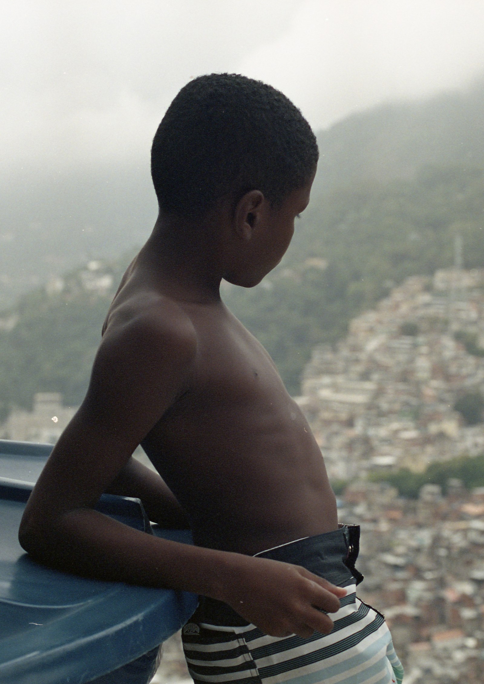 un chico sin camisa asomado sobre un tanque de agua, el cerro en la neblina