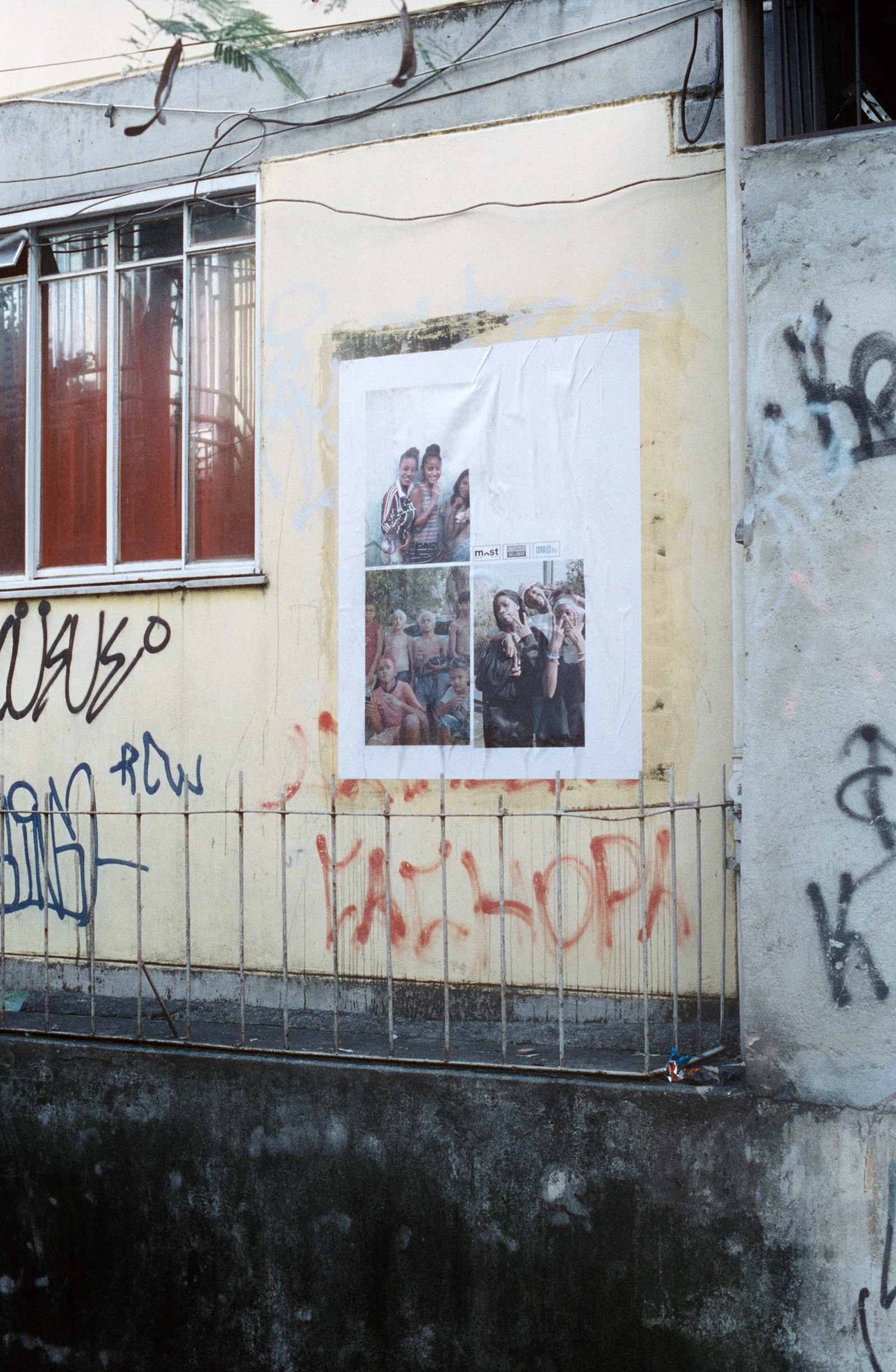 une affiche de trois portraits sur un mur jaune, au-dessus d’une grille