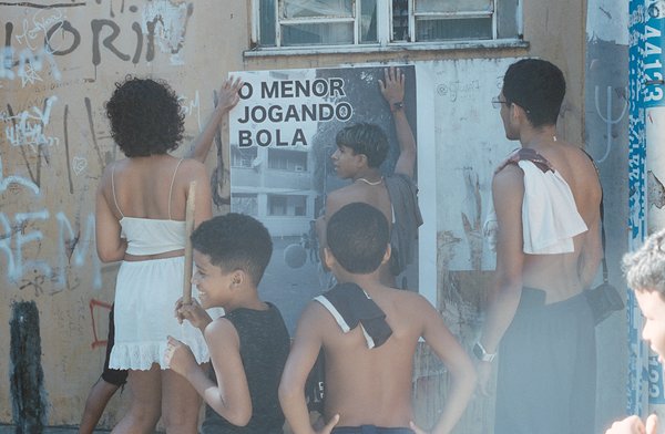 une jeune femme et des enfants collent une grande affiche en noir et blanc sur un mur