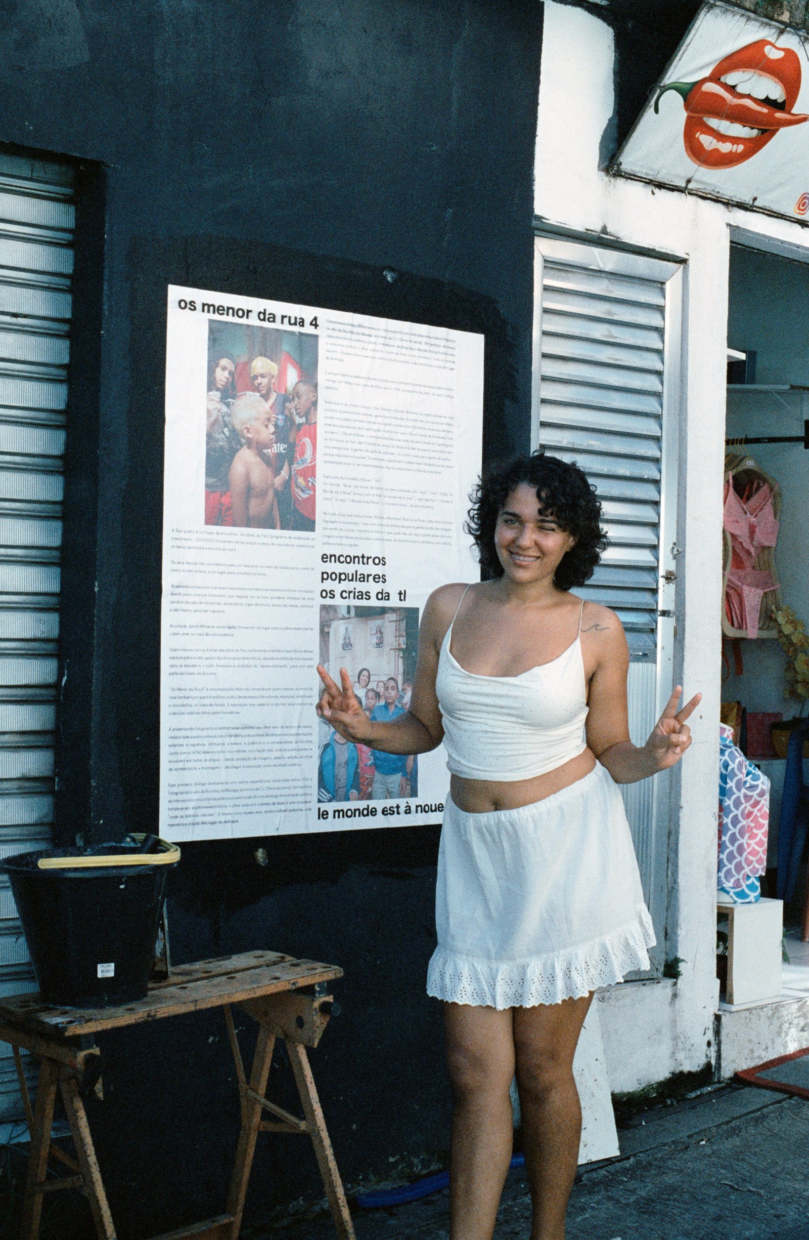 une jeune femme sourit et fait le V de la victoire devant l’affiche « os menor da rua 4 »